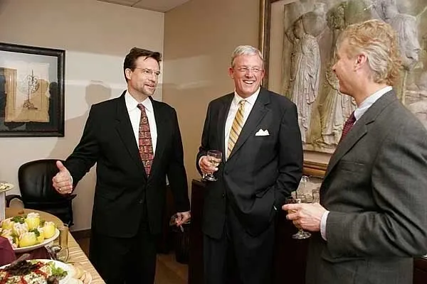 Three men in suits and ties standing next to a table.