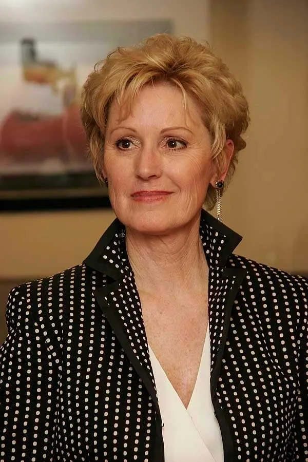 A woman with short blonde hair wearing a black and white polka dot jacket.