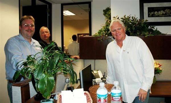 Three men standing in a room with plants.